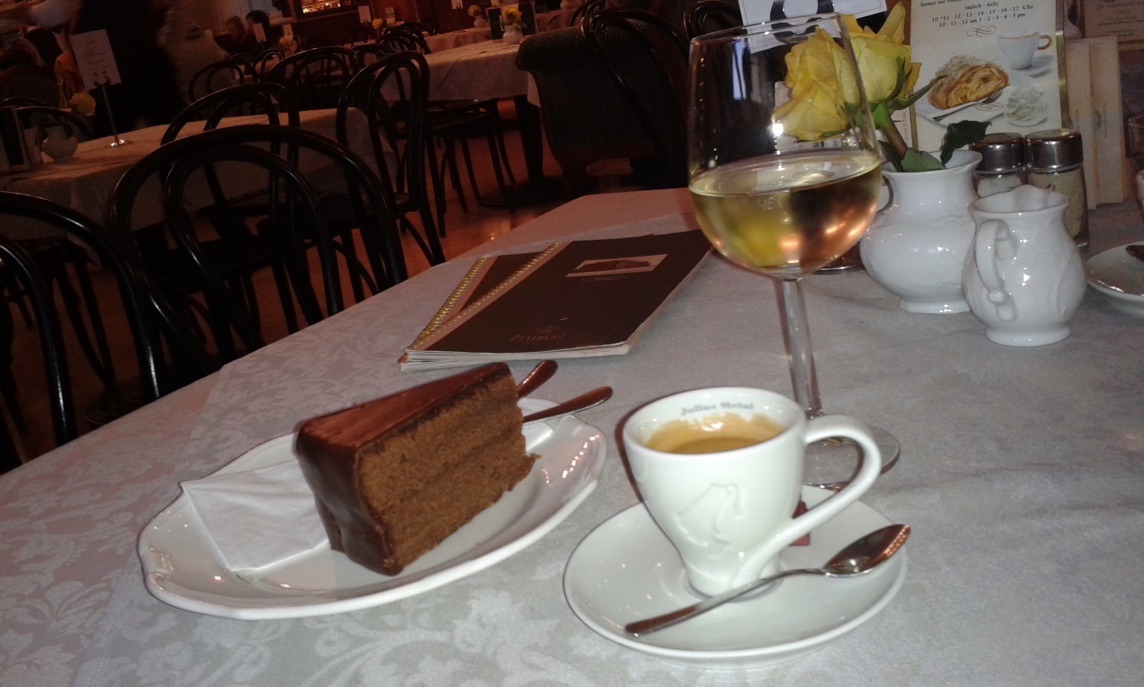 Šálek kávy, sachr dort a sklenka bílého vína ve vídeňské kavárně